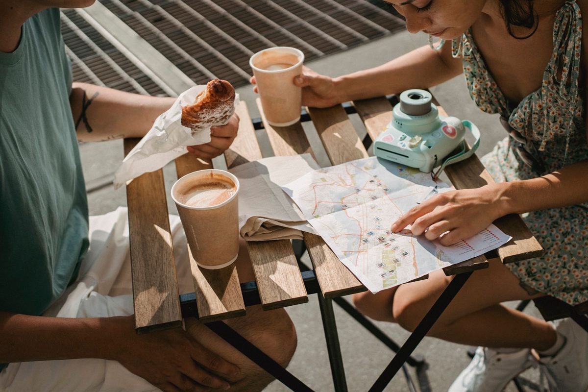 Two travellers with coffee and croissants planning a route on a paper map