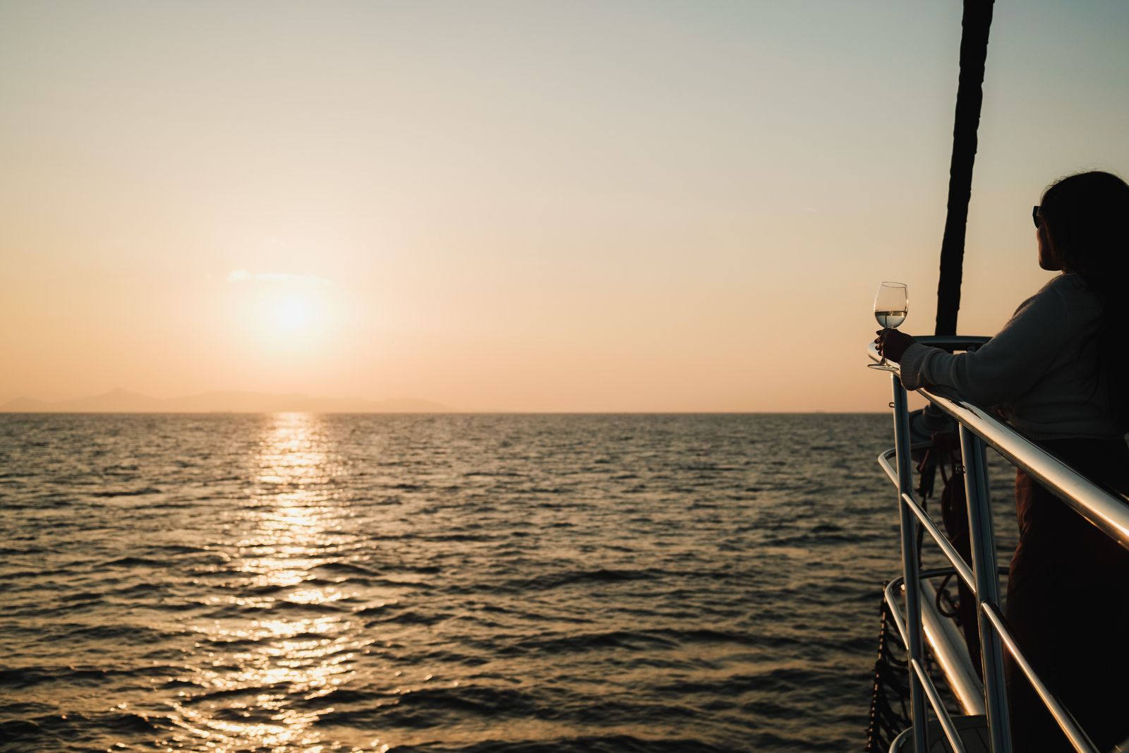 A traveller with a glass of wine at a cruise ship rail watching the sun set over the sea, a trip arranged by a personal cruise planner