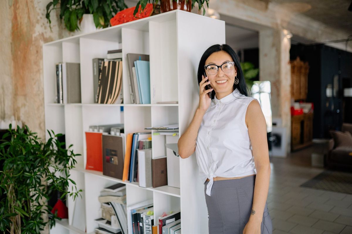 A businesswoman smiling during a phone call beside a bookshelf