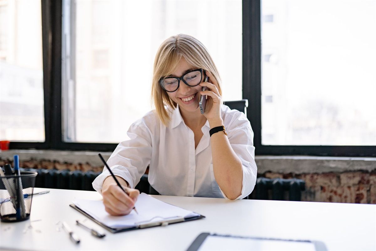 A smiling advisor on the phone writing notes at a desk
